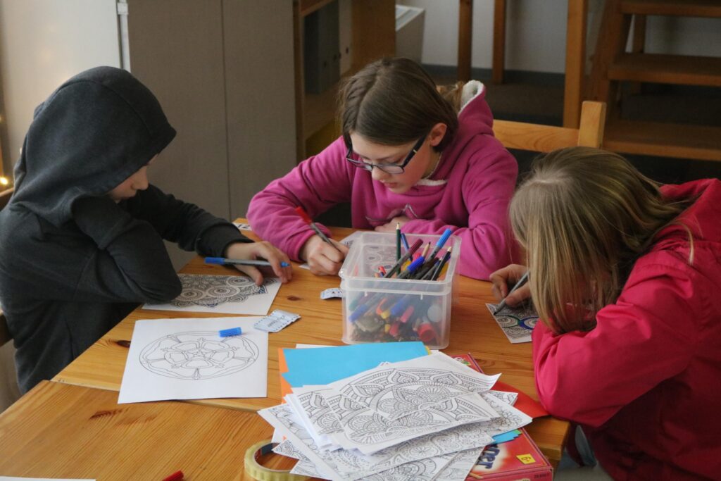 Kinder sitzen an einem Tisch und malen mit Farben in Ausmalbildern.