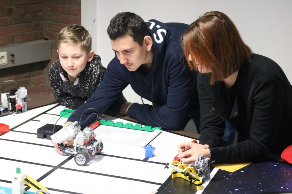 Drei Personen arbeiten gemeinsam an einem Roboter-Projekt am Tisch.