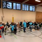Die Schülerband spielt in einer Turnhalle. Alle tragen blaue T-Shirts.