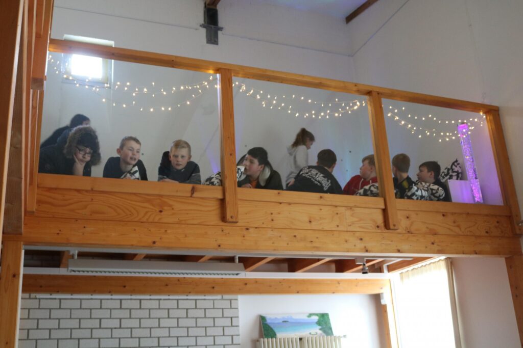 Schüler sitzen an Tischen auf einer Empore, Lichterdekoration im Hintergrund.