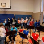 Schülerinnen und Schüler stehen in einem Musikraum und proben gemeinsam.