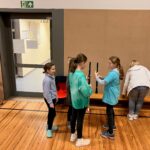 Vier Kinder stehen in einer Turnhalle und halten Flöten.
