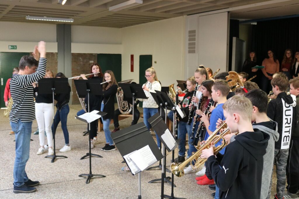 Schüler spielen in einem Musikraum gemeinsam Instrumente unter der Leitung eines Dirigenten.