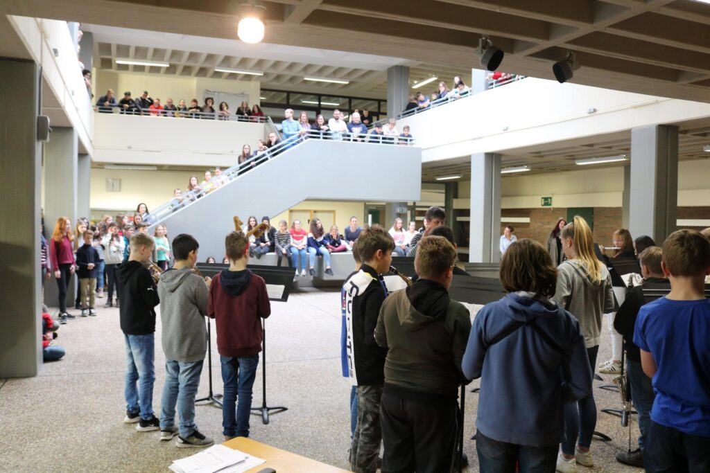 Schüler treten in einer Aula auf, Publikum sitzt auf den Rängen.