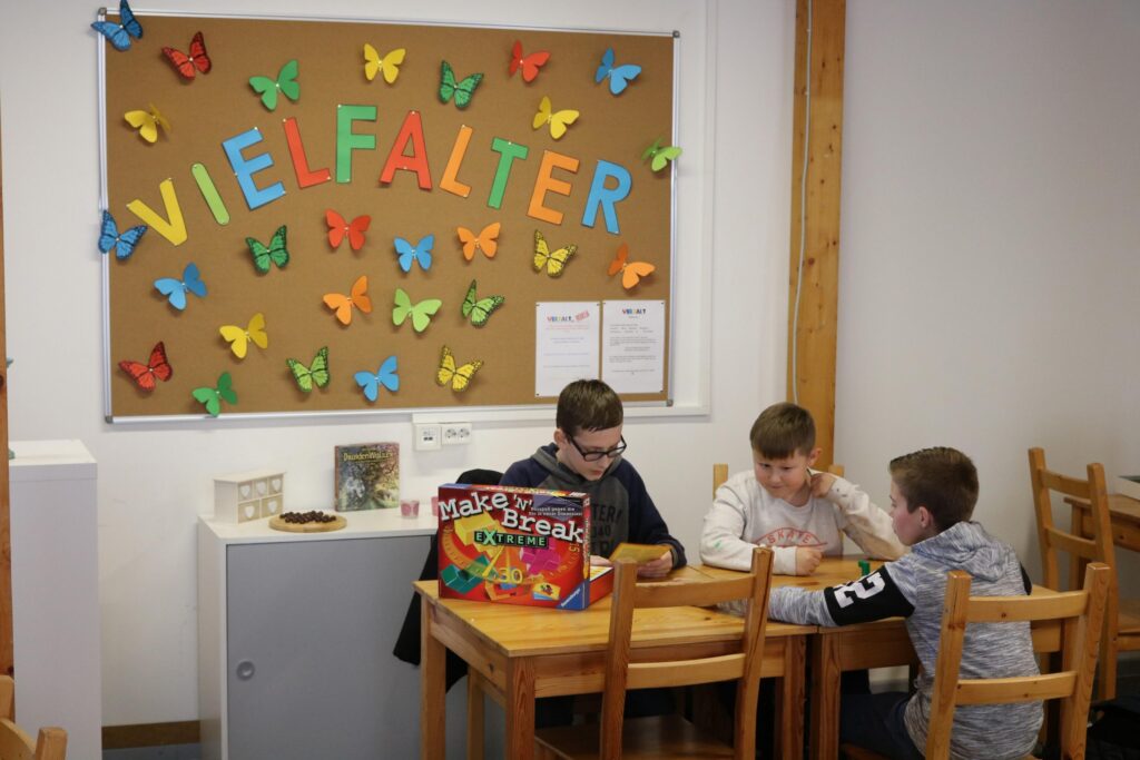 Drei Schüler sitzen an einem Tisch vor einer bunten Wand mit Schmetterlingen.