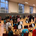 Probenveranstaltung in einer Turnhalle mit vielen Schülern und Instrumentenständern.