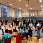 Viele Kinder stehen in einer Schule in einem großen Raum mit Holzfußboden und Basketballkorb.
