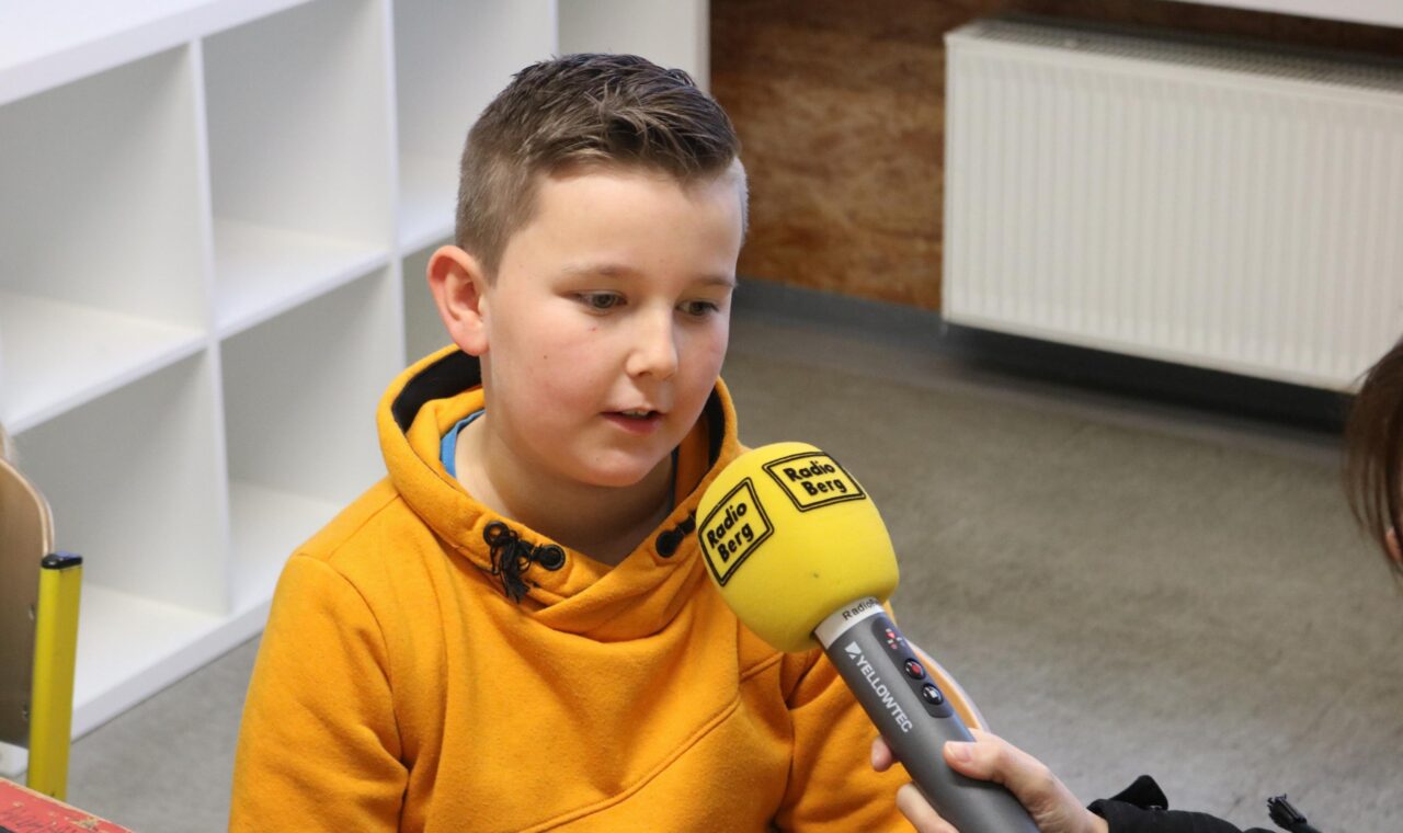Ein Junge in einem gelben Hoodie spricht mit einer Person, die ein Mikrofon hält.