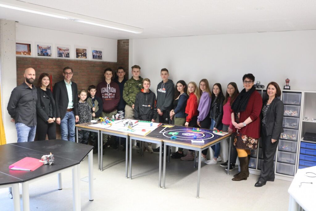 Gruppe von Schülern und Lehrern in einem Klassenzimmer mit Projekten auf Tischen.