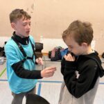Zwei Jungen in einer Sporthalle, einer zeigt etwas dem anderen.