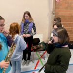 Schülerinnen stehen in einer Halle und üben mit Instrumenten.