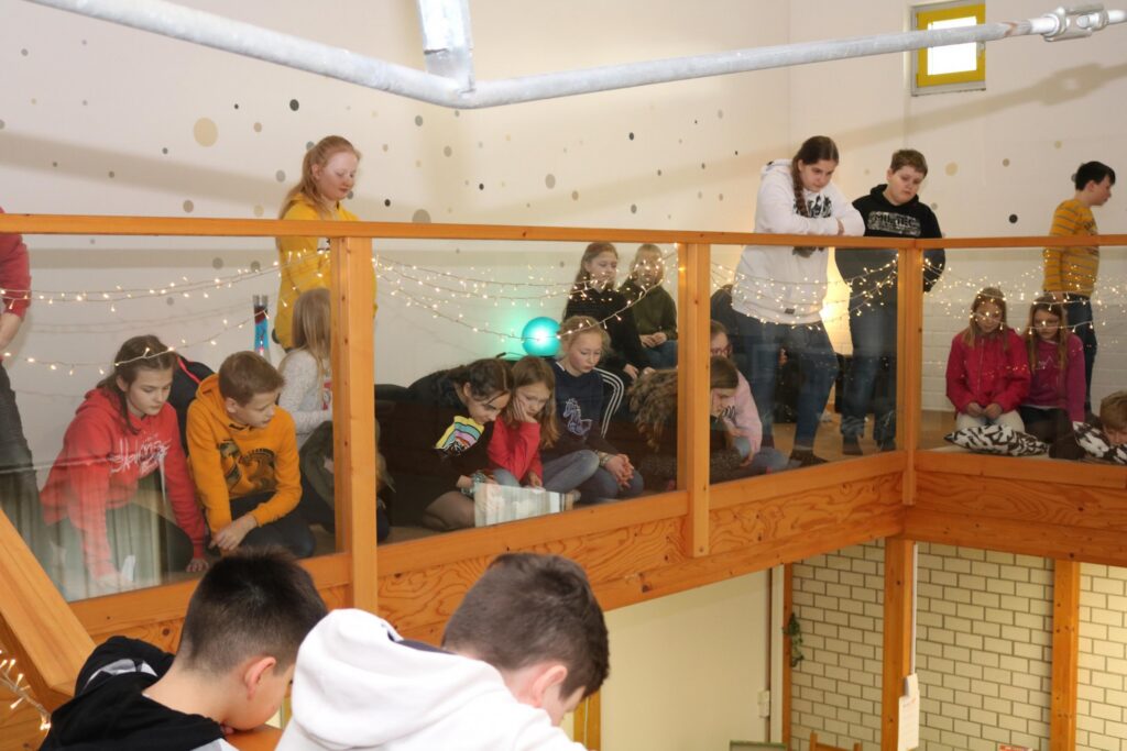 Schülerinnen und Schüler sitzen und stehen auf einer Galerie, schauen nach unten.