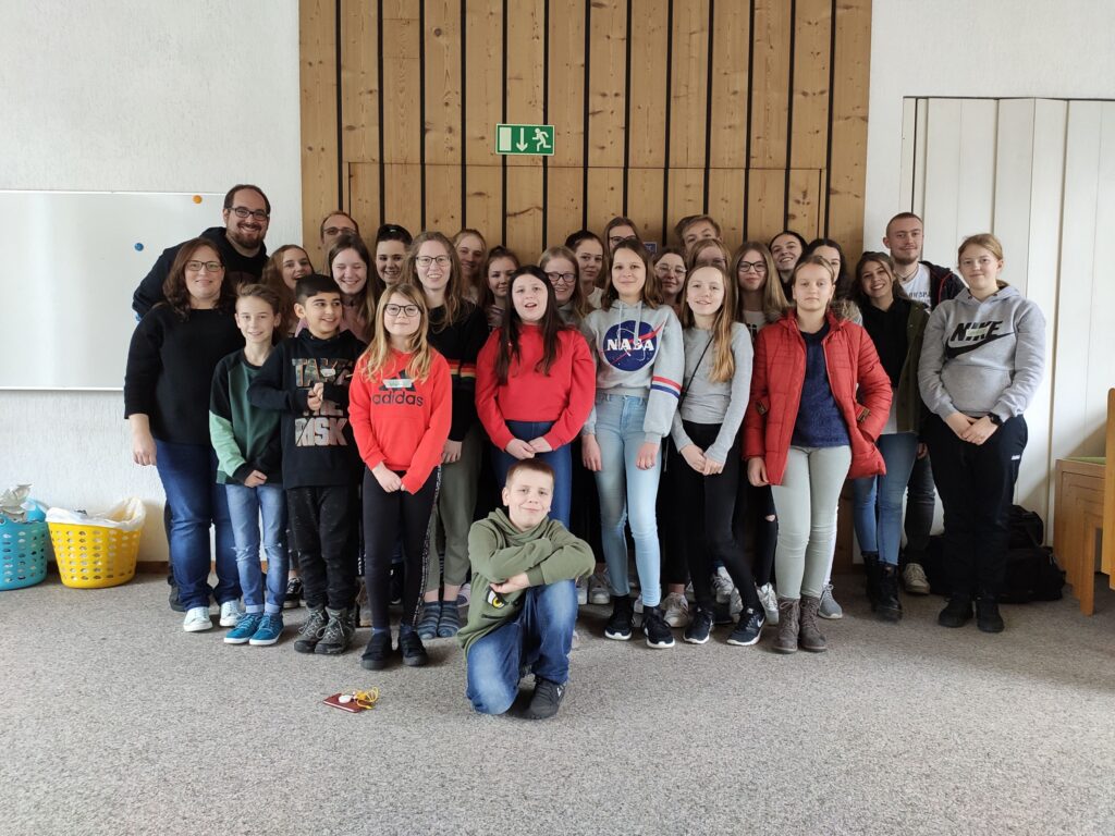 Gruppe von Schülern und Lehrern in einem Raum, alle lächeln in die Kamera.
