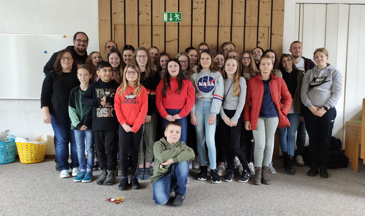 Gruppe von Schülern und Lehrern in einem Raum, alle lächeln in die Kamera.
