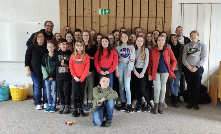 Gruppe von Schülern und Lehrern in einem Raum, alle lächeln in die Kamera.