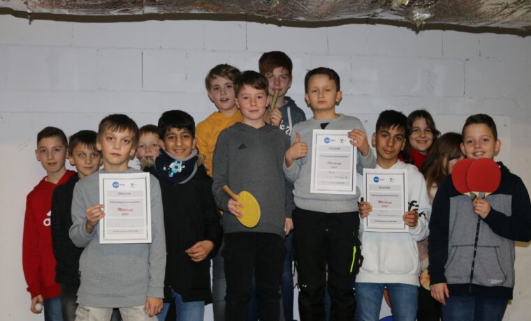 Gruppe von Schülern mit Urkunden und Tischtennisschlägern in einem Raum.