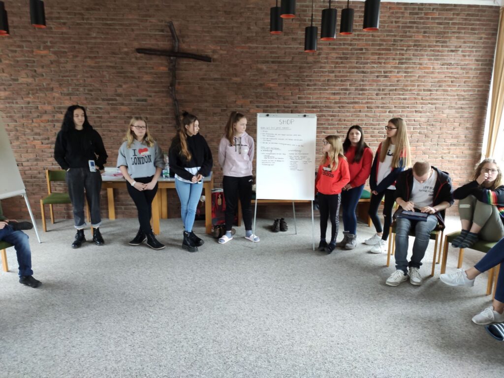 Gruppe von Jugendlichen steht im Kreis in einem Raum mit gemauerter Wand.