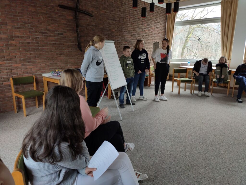 Schülerinnen und Schüler präsentieren an einem Flipchart in einem Gruppenraum.