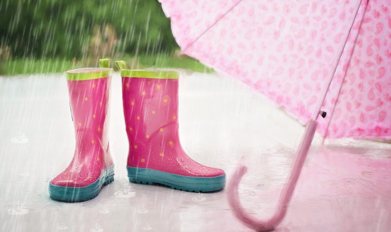 Rosa Gummistiefel stehen unter einem pinken Regenschirm im Regen.