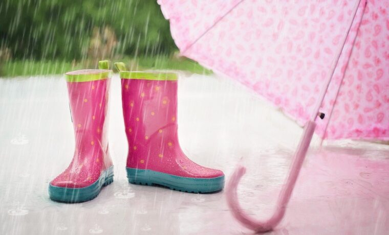 Rosa Gummistiefel stehen unter einem pinken Regenschirm im Regen.
