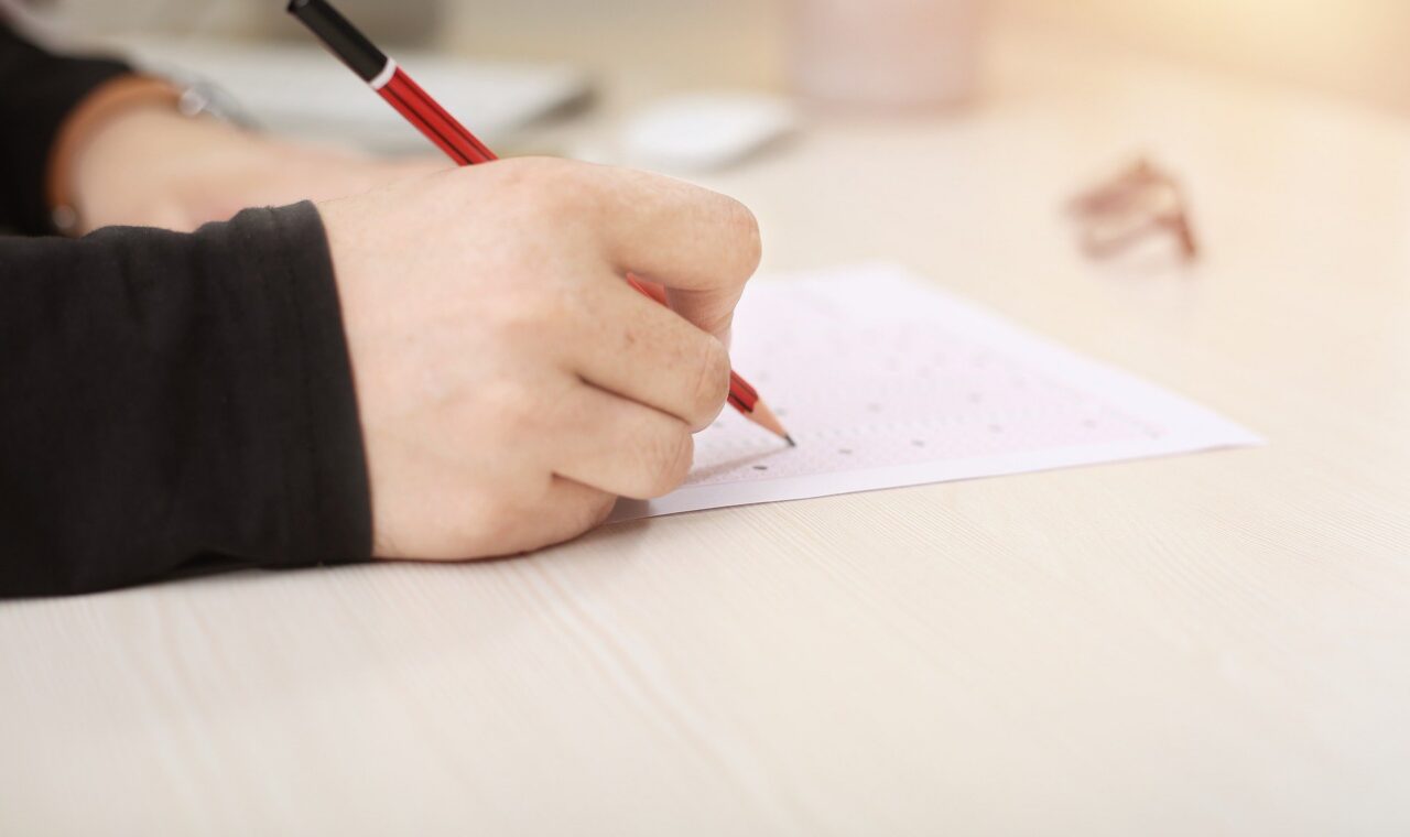 Eine Hand schreibt mit einem roten Stift auf einem Blatt Papier.