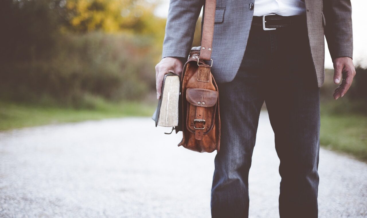 Lehrer mit Tasche und Buch steht auf einem Weg.
