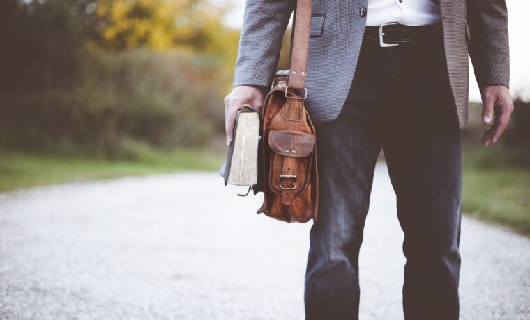 Lehrer mit Tasche und Buch steht auf einem Weg.