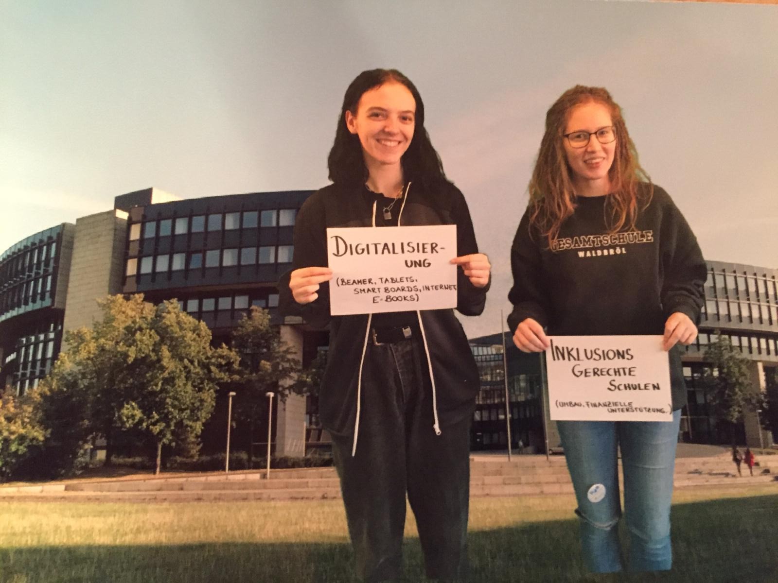 Zwei Schüler halten Schilder mit den Wörtern "Digitalisieren" und "Innovationen" vor einem Gebäude.