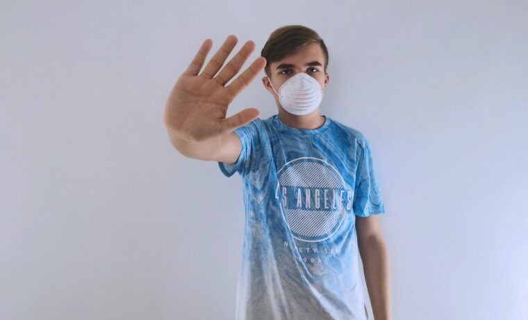 Junger Mann mit Mundschutz hält Hand zur Abwehr.