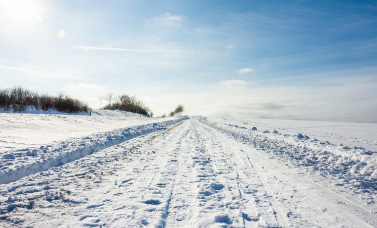 Schneebedeckte Straße unter blauem Himmel. Eindeutige Fußabdrücke im Schnee.