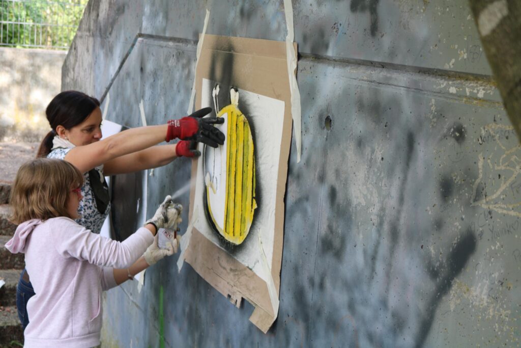 Zwei Personen sprayen ein Kunstmotiv an eine Wand.