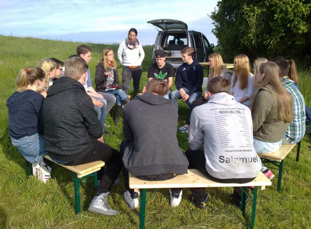 Gruppe von Jugendlichen sitzt auf Bänken im Freien und diskutiert.