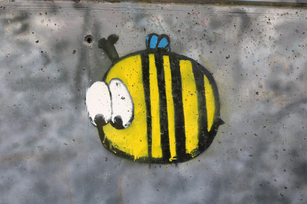 Graffiti eines gelben Bienenmotivs mit großen Augen auf grauem Hintergrund.