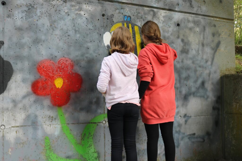 Zwei Mädchen sprühen ein farbiges Graffiti an eine Wand.
