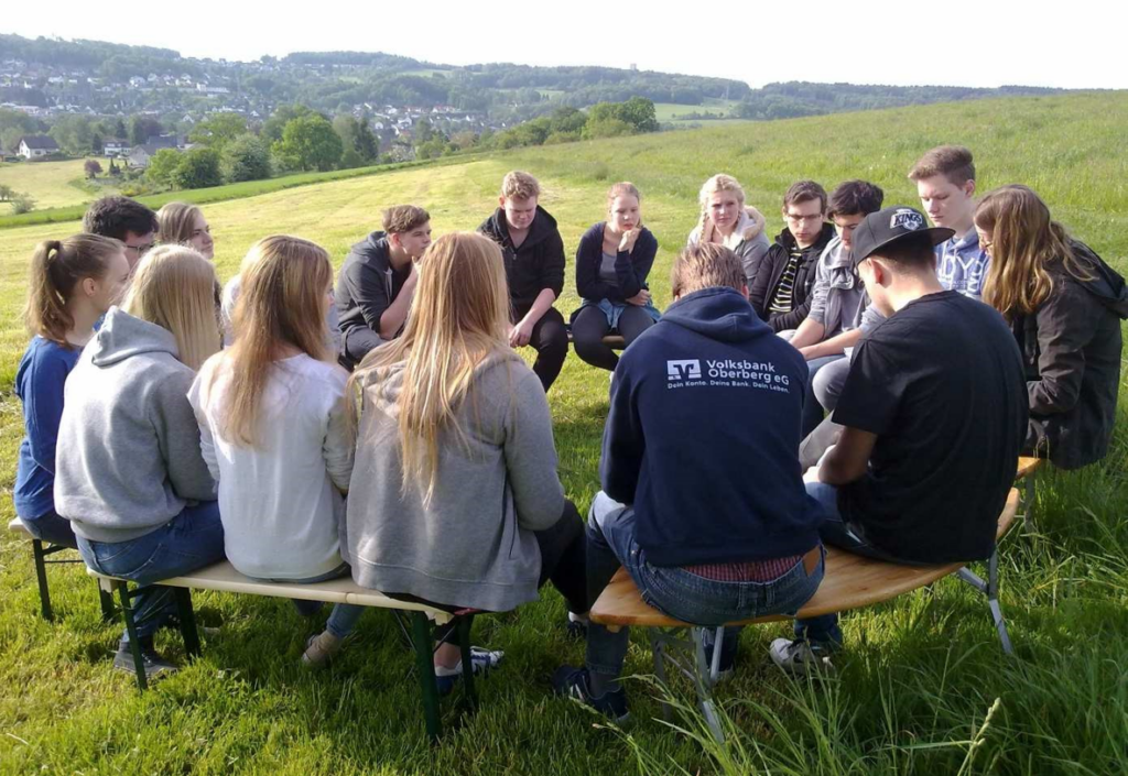 Gruppe von Jugendlichen sitzt im Kreis auf einer Wiese und diskutiert.