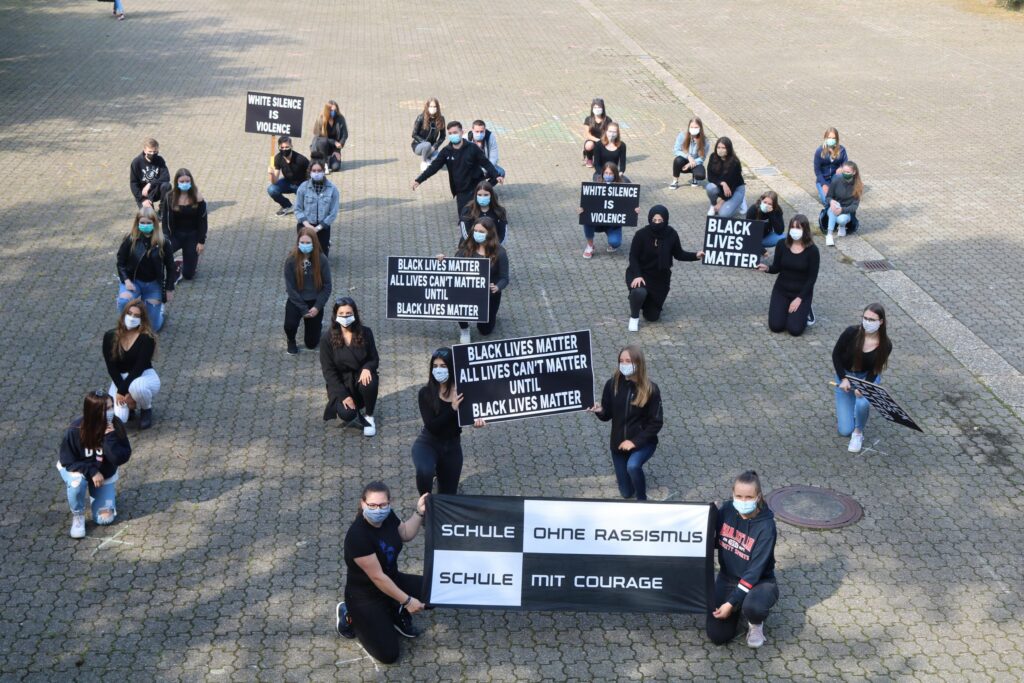 Schülerinnen und Schüler knien auf dem Schulhof mit Plakaten für Gerechtigkeit.