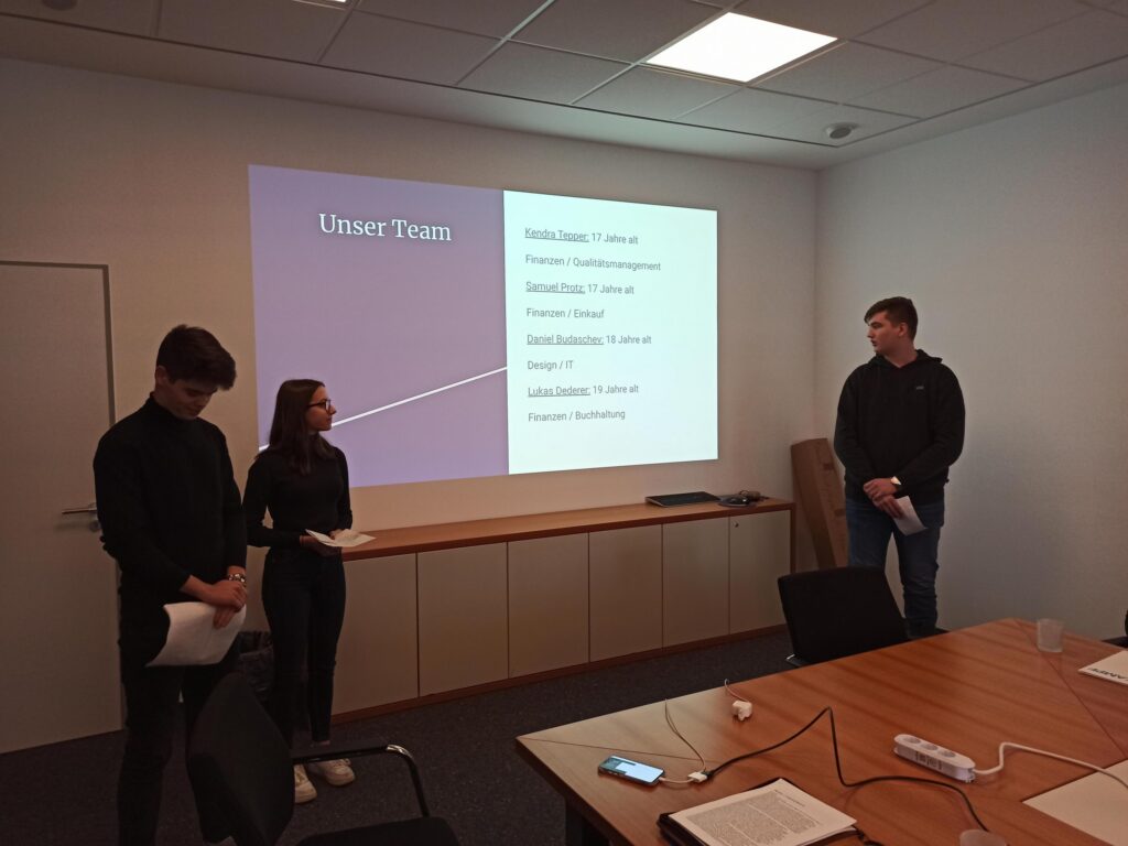 Präsentation in einem Besprechungsraum mit drei Schülern und einer Folie.