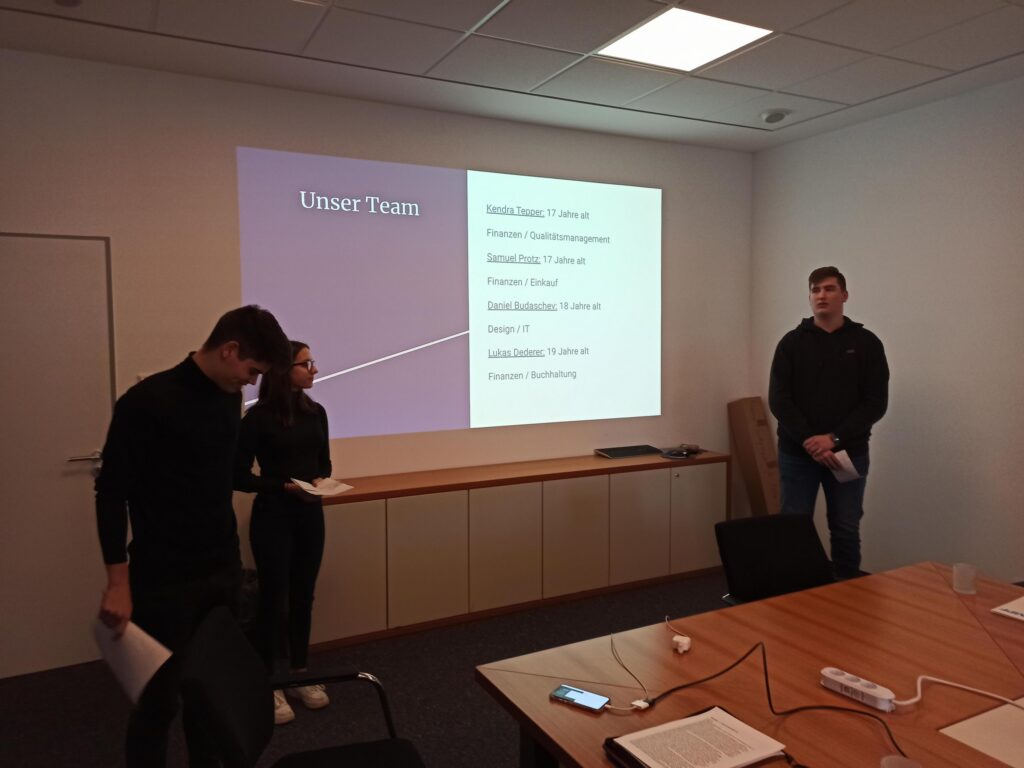 Zwei Schüler präsentieren in einem Konferenzraum vor einer Leinwand.