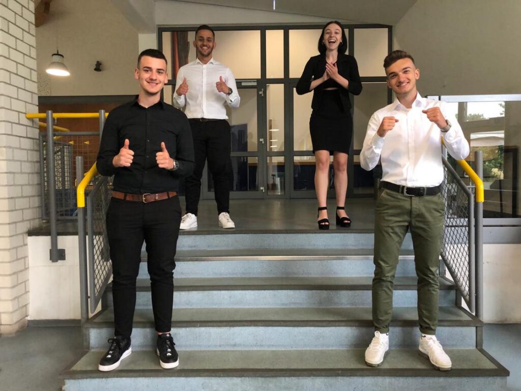 Vier Personen stehen auf einer Treppe und zeigen Daumen hoch.
