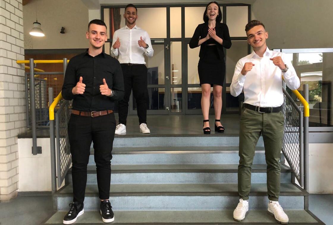 Vier Personen stehen auf einer Treppe und zeigen Daumen hoch.