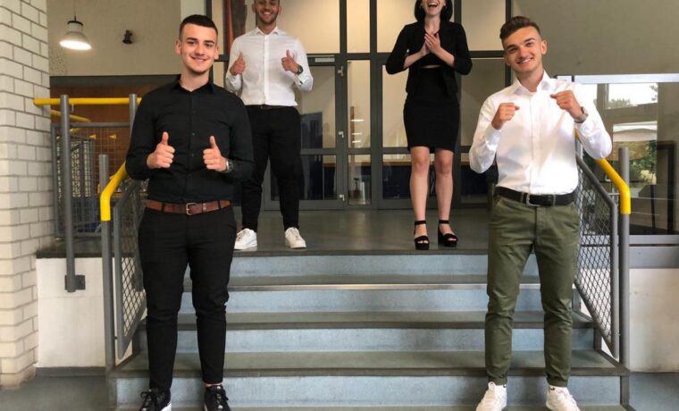 Vier Personen stehen auf einer Treppe und zeigen Daumen hoch.
