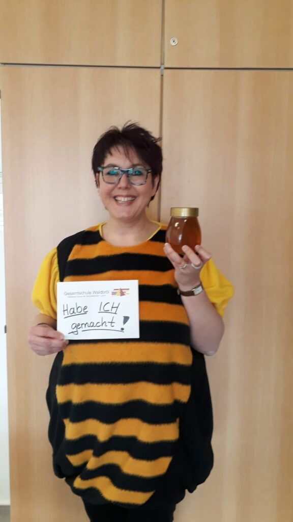 Person in Bienenkostüm hält ein Honigglas und ein Schild mit „Hab' ich geschenkt!“