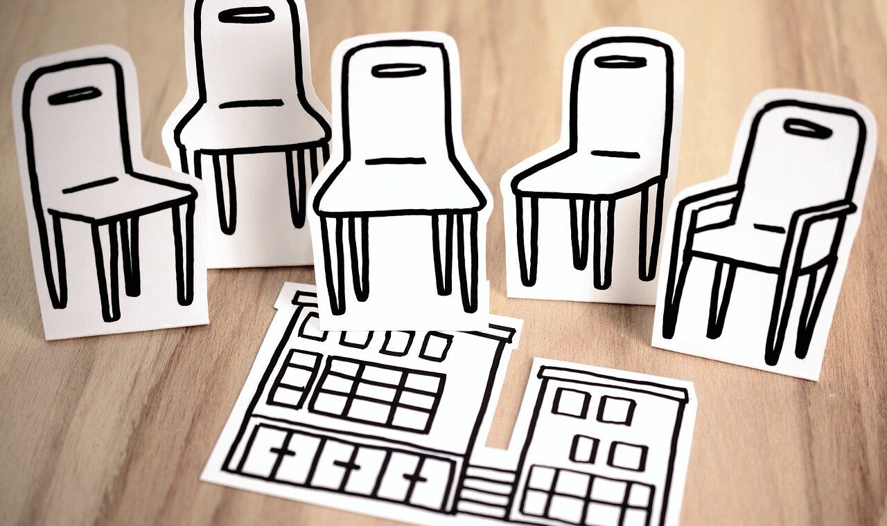 Papierfiguren von Stühlen und einem Gebäude auf einem Holztisch.