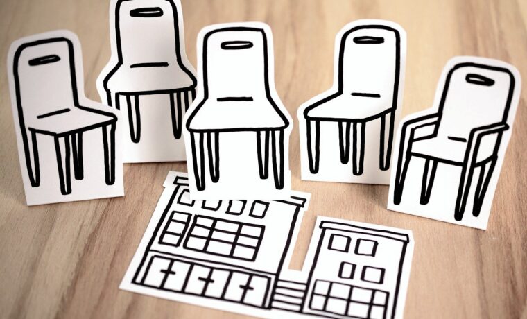 Papierfiguren von Stühlen und einem Gebäude auf einem Holztisch.