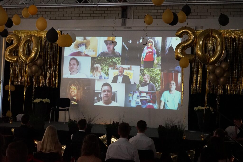 Feierliche Bühne mit einem Projektor, der Bilder von Personen zeigt, umgeben von Ballons.
