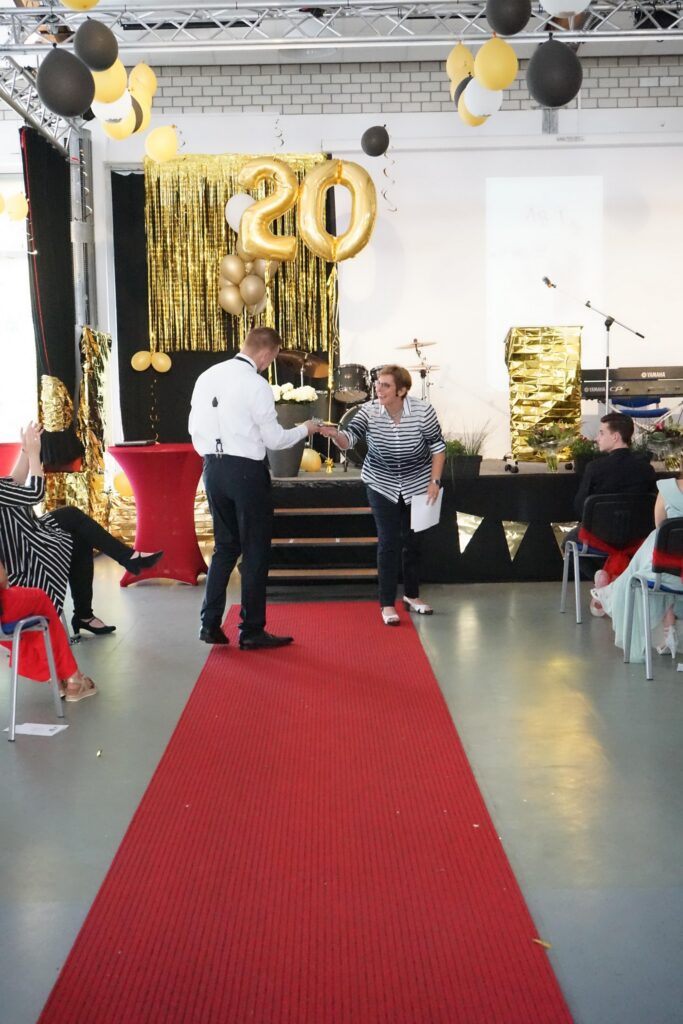 Roter Teppich mit Gästen, goldene Dekoration und Bühne im Hintergrund.