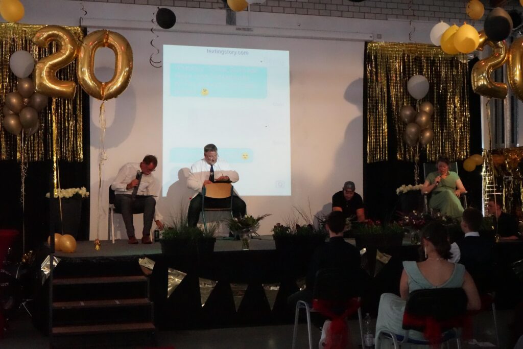 Veranstaltung mit einer Bühne, Ballons und dekorativen Elementen. Zuschauer sitzen im Publikum.