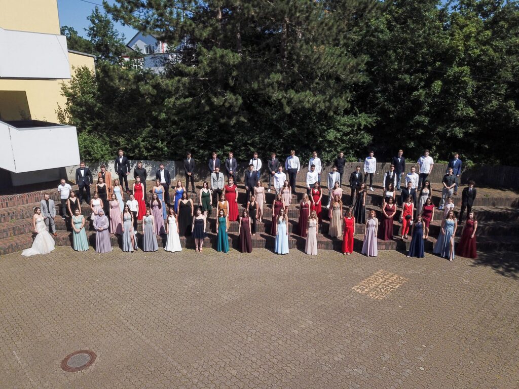 Schülergruppe in Formationen, elegant gekleidet, vor einer Schule.