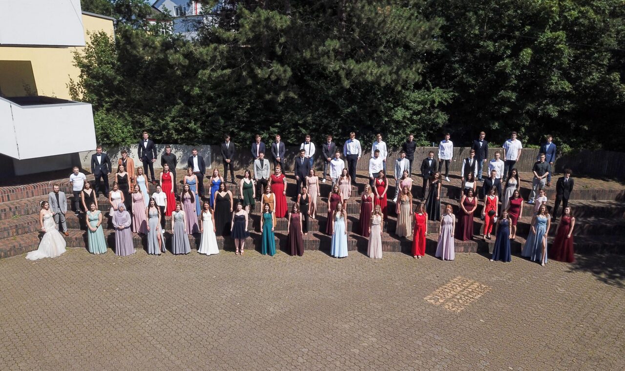 Schülergruppe in Formationen, elegant gekleidet, vor einer Schule.