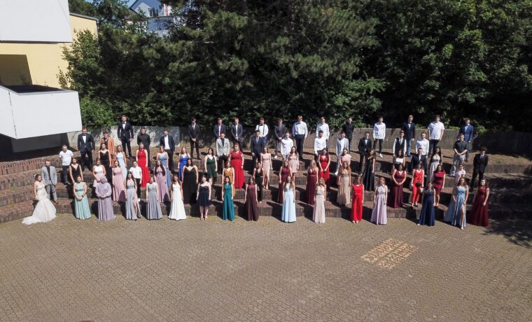 Schülergruppe in Formationen, elegant gekleidet, vor einer Schule.